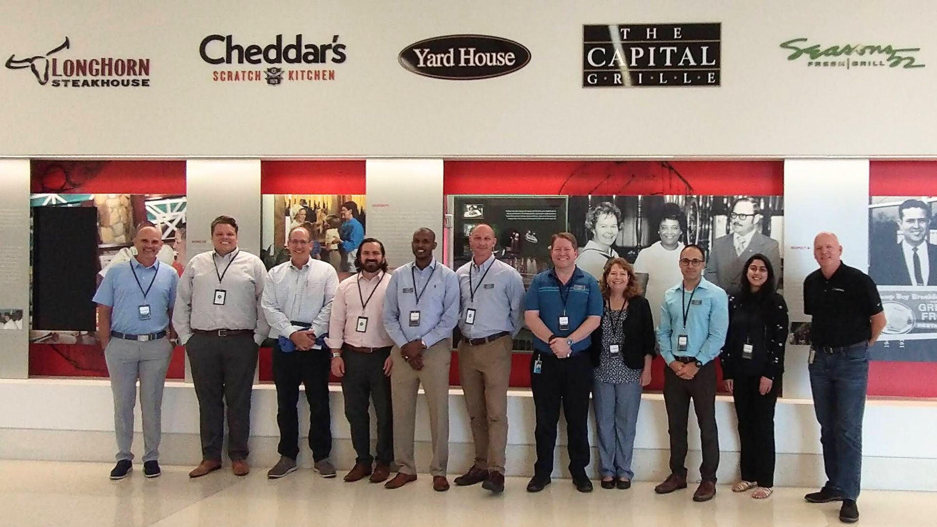 A group of professionals in front of a wall with branding for Longhorn Steakhouse, Yard House, Capital Grille, and Seasons 52