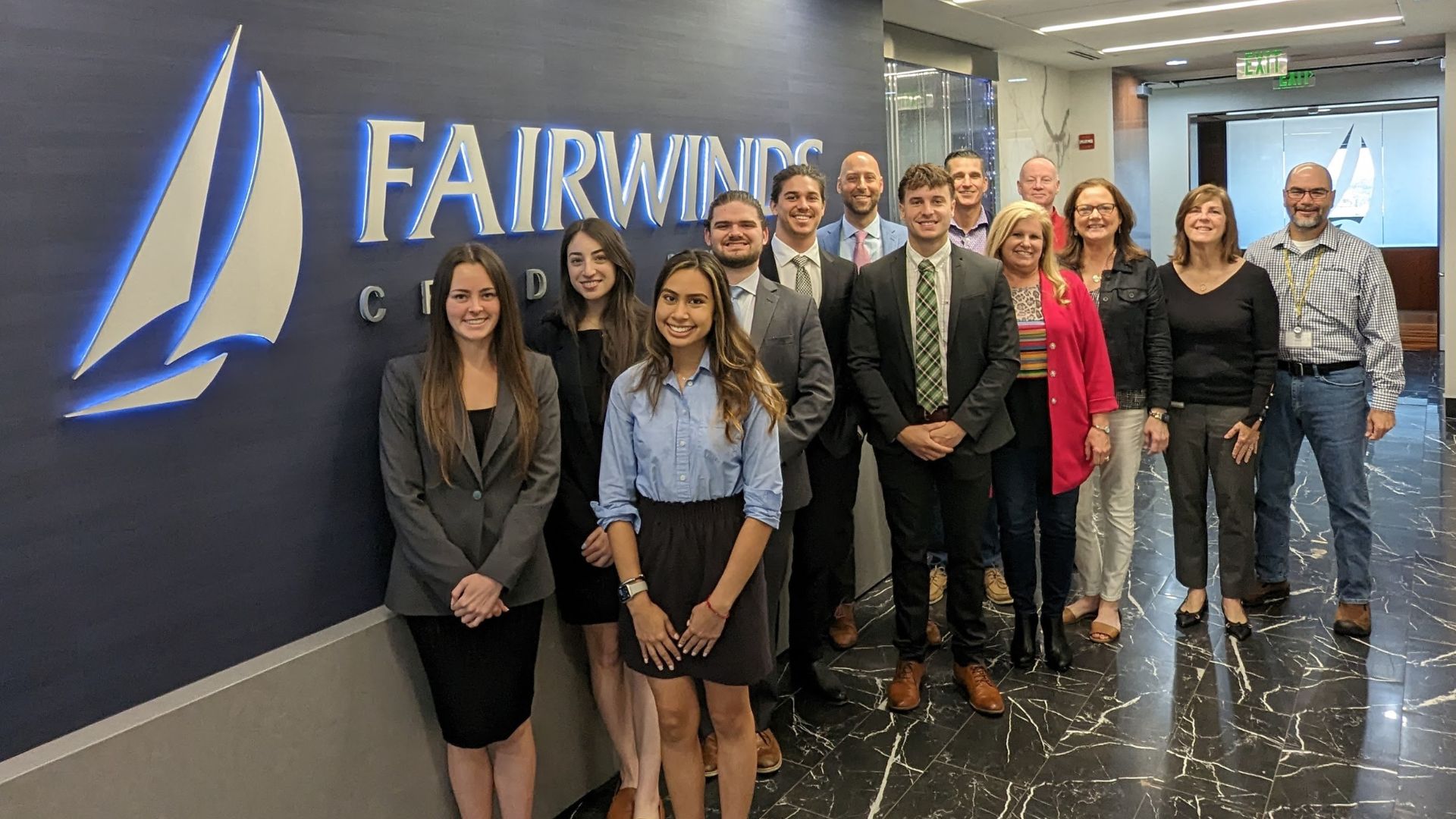 Group of students and Fairwinds Credit Union professionals pose in front of a corporate logo during a career services visit