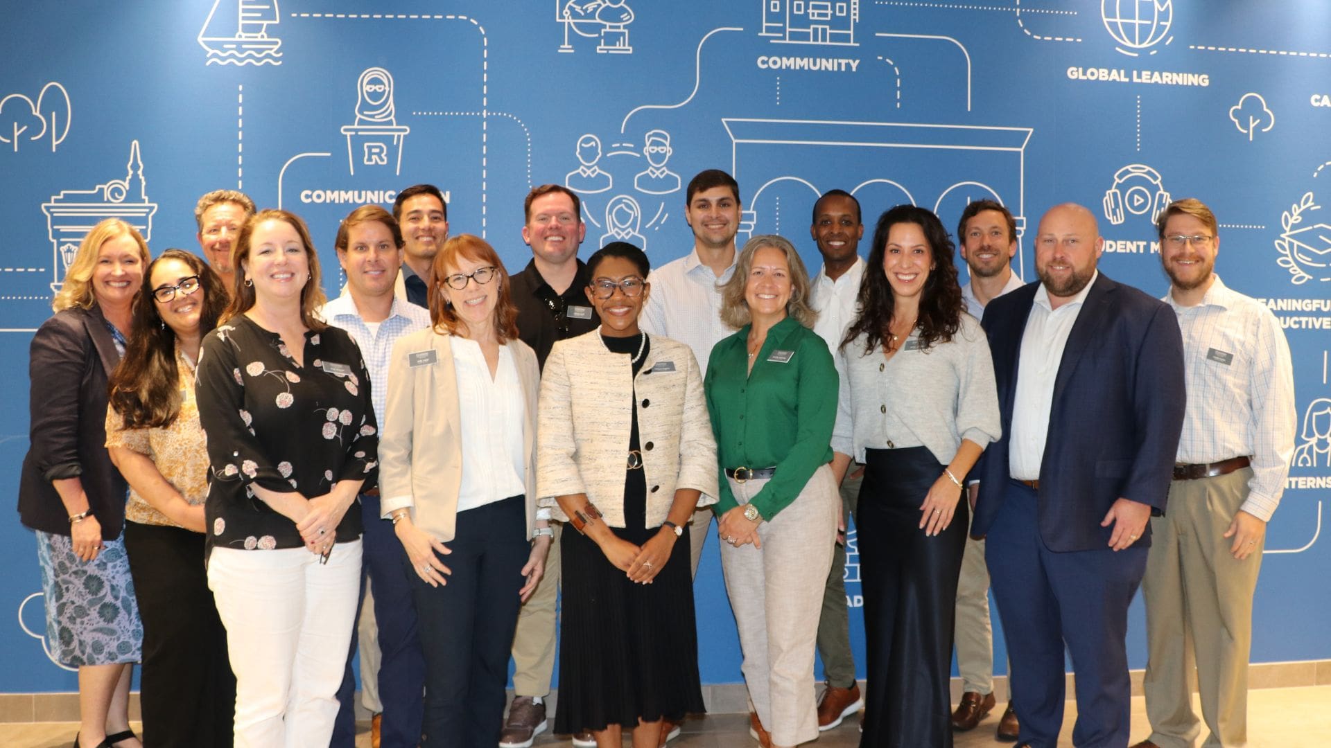 a group of twenty executive MBA students stand in front of a blue wall