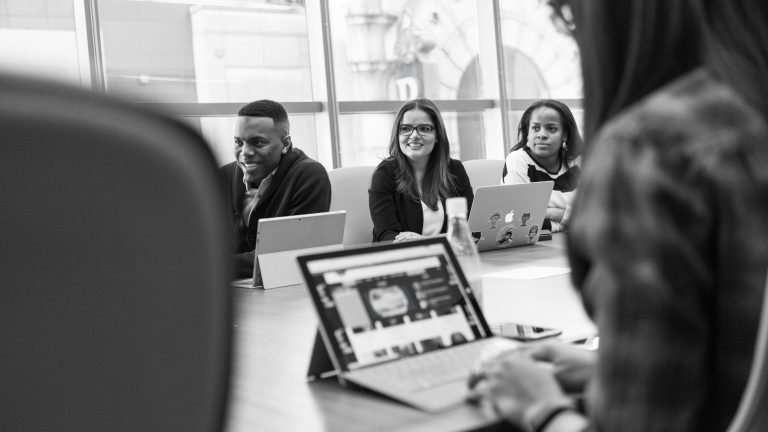 Group of professionals working on laptops in a meeting room (black and white).
