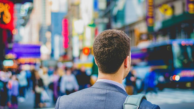 Man in a suit with a shoulder bag looking out at a busy city street.