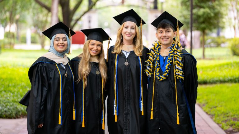 Four MBA graduates smiling in caps and gowns.