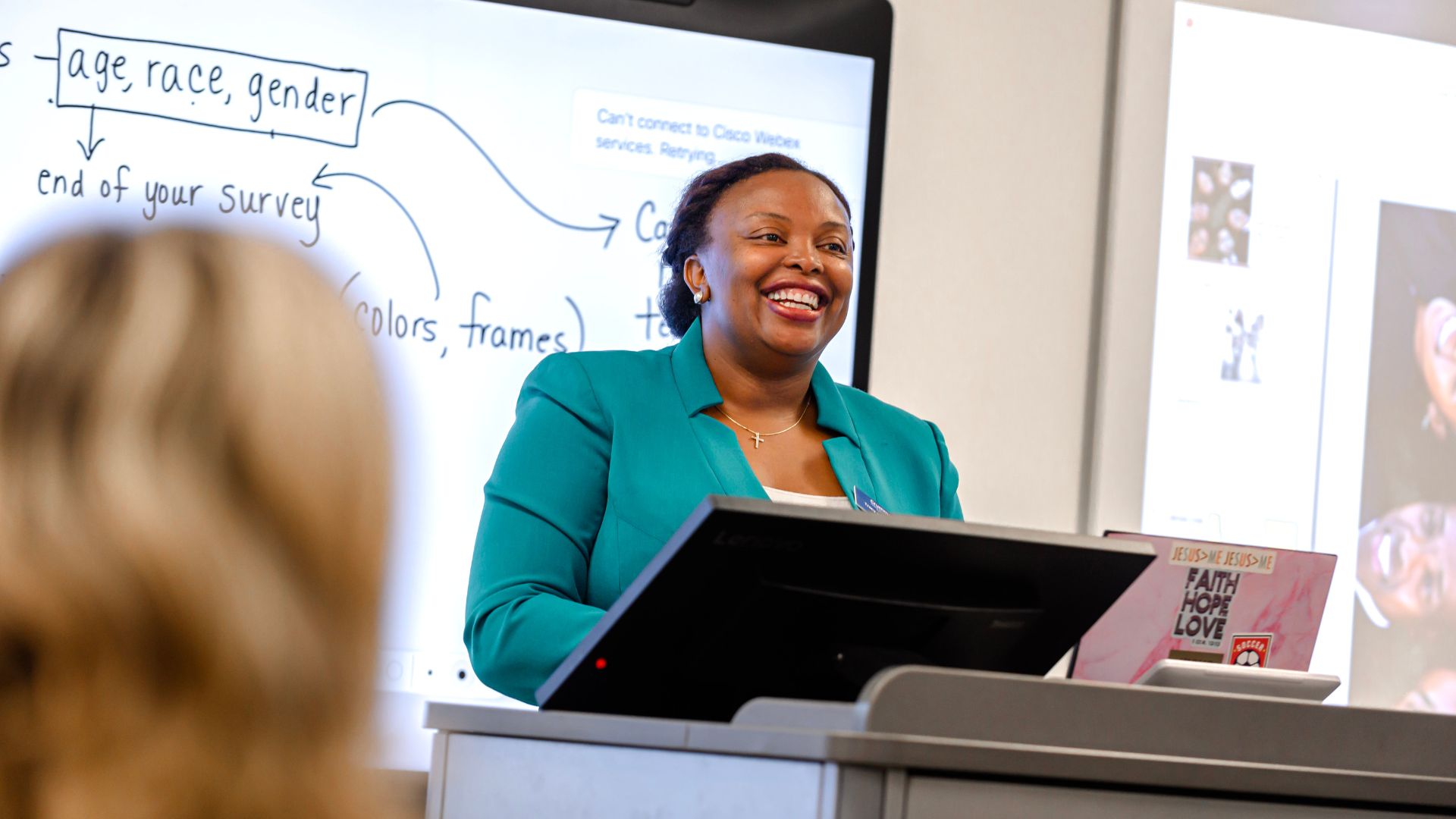 tracy kizer smiling in a green jacket standing in front of the class